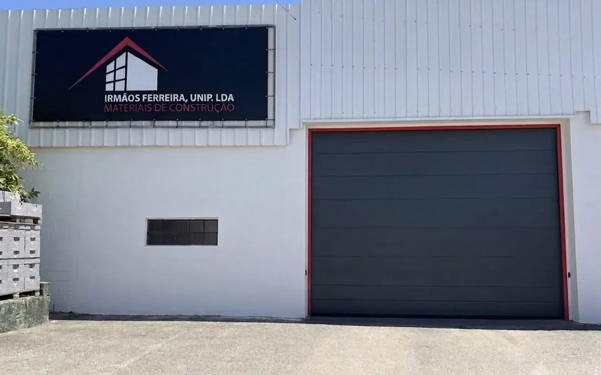 Fachada do armazém da Irmãos Ferreira em Arada, Ovar, com a placa da empresa e o portão de moldura vermelha.
